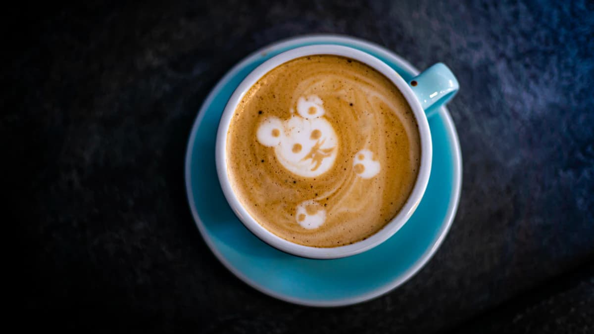 A blue coffee cup with playful latte art on a dark tabletop