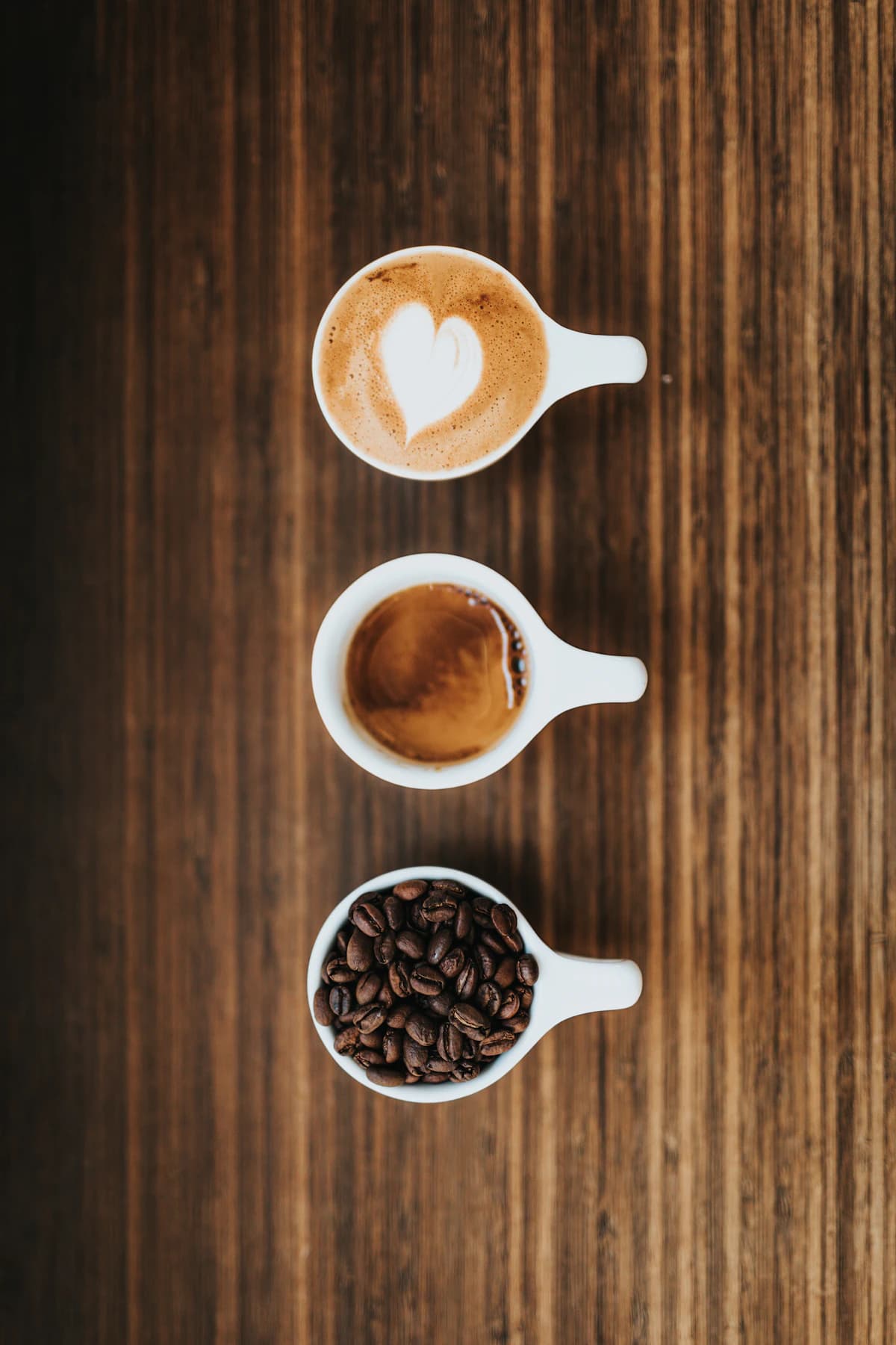 Three white cups with coffee beans, black coffee, and latte art