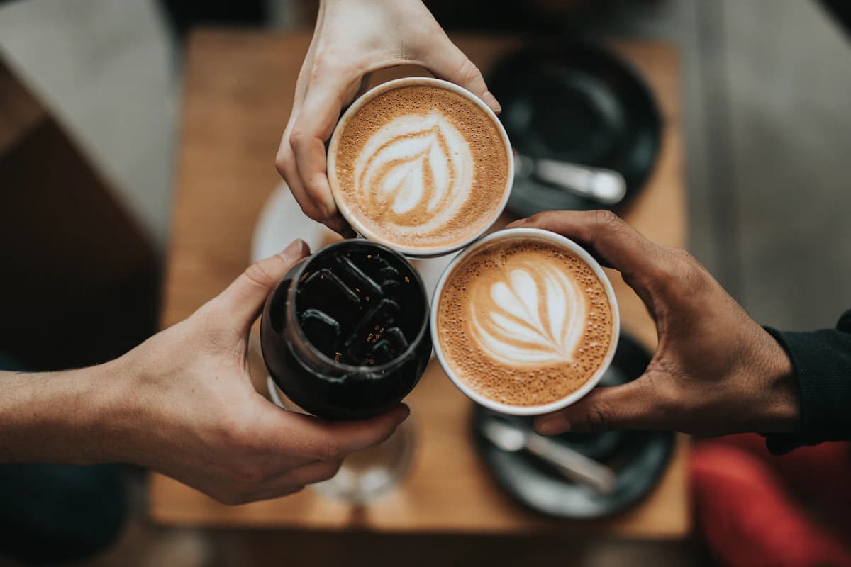 Three people bringing their coffee cups together for a cheerful toast